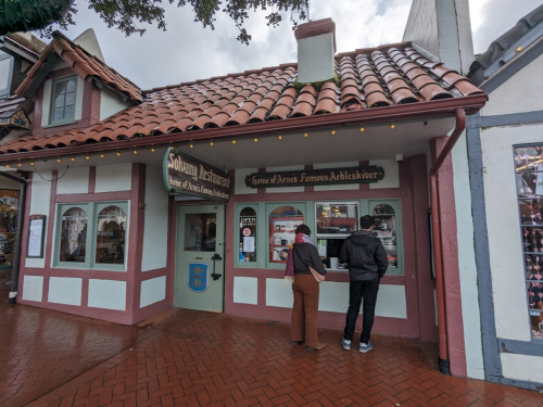 A quaint building with a tiled roof and colorful signage, featuring two people ordering at a window.