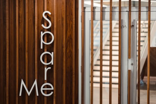 Wooden wall with the text "Spare Me" and a glass door leading to a staircase in the background.