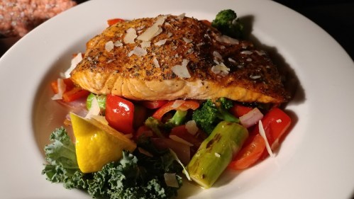 A beautifully plated salmon fillet on a bed of colorful vegetables, garnished with lemon and herbs.