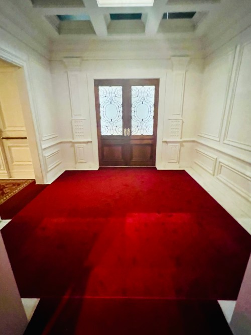 A spacious entryway with a red carpet and elegant double doors featuring decorative glass panels.