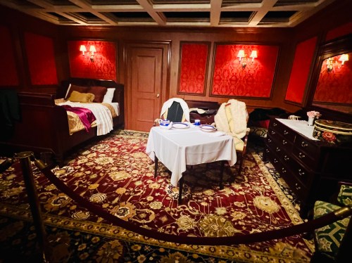 A cozy, elegantly decorated bedroom with a bed, dining table, and rich red walls, featuring vintage furnishings.