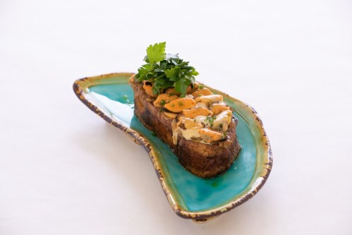 A slice of toasted bread topped with creamy seafood and garnished with fresh herbs, served on a decorative plate.