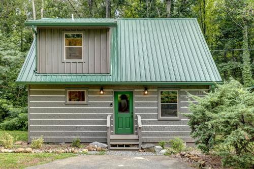 A cozy cabin with a green metal roof, surrounded by trees, featuring a front porch and landscaped garden.