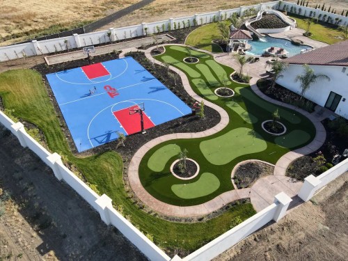 Aerial view of a backyard featuring a basketball court, putting green, and a pool area surrounded by landscaping.