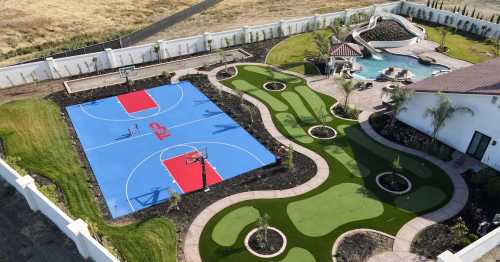 Aerial view of a backyard featuring two basketball courts, a pool, and landscaped green areas.