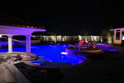 A beautifully lit pool area at night, featuring colorful lights, lounge chairs, and a serene atmosphere.