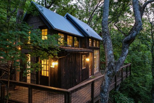A cozy treehouse nestled among trees, featuring large windows and warm lights, with a wooden deck.