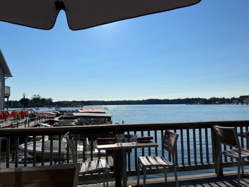 A serene lakeside view from a deck, featuring boats docked and a clear blue sky.