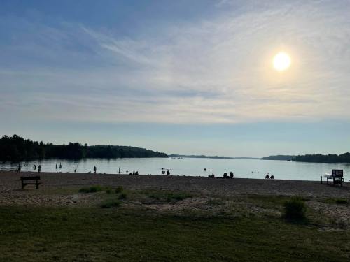 A serene lakeside scene at sunset, with people enjoying the water and benches along the shore.