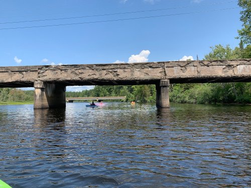 A view of a bridge over a river, with kayakers paddling beneath it surrounded by lush greenery.