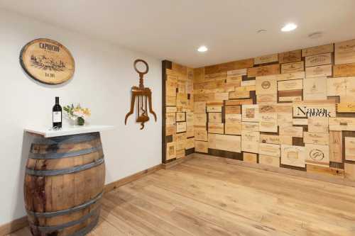 A cozy wine cellar featuring a wooden barrel, a bottle of wine, and a wall adorned with wooden wine box labels.