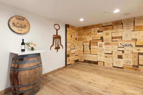A cozy wine cellar featuring a wooden barrel, a bottle of wine, and a wall adorned with wooden wine box labels.