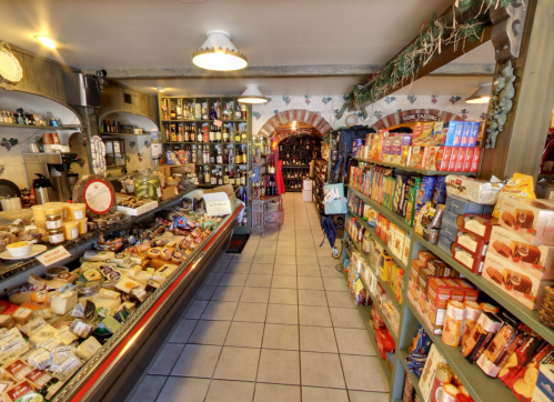 A cozy grocery store aisle filled with various cheeses, snacks, and beverages, with warm lighting and rustic decor.