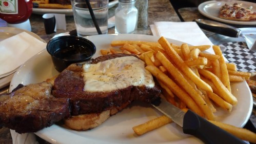 A plate with a grilled steak topped with butter, served with a side of golden French fries.