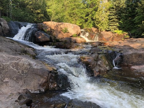 A serene waterfall cascading over rocky terrain, surrounded by lush green trees and a peaceful natural setting.