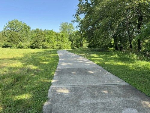 A smooth, winding concrete path through a lush green landscape under a clear blue sky.