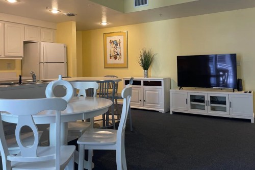 Bright, modern living space featuring a dining table, kitchen area, and a TV unit against a yellow wall.