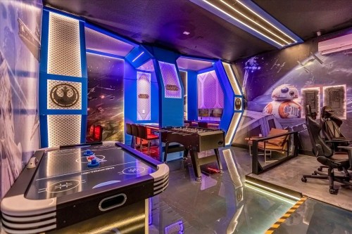 A futuristic game room with neon blue lighting, featuring air hockey, foosball, and sci-fi themed decor.