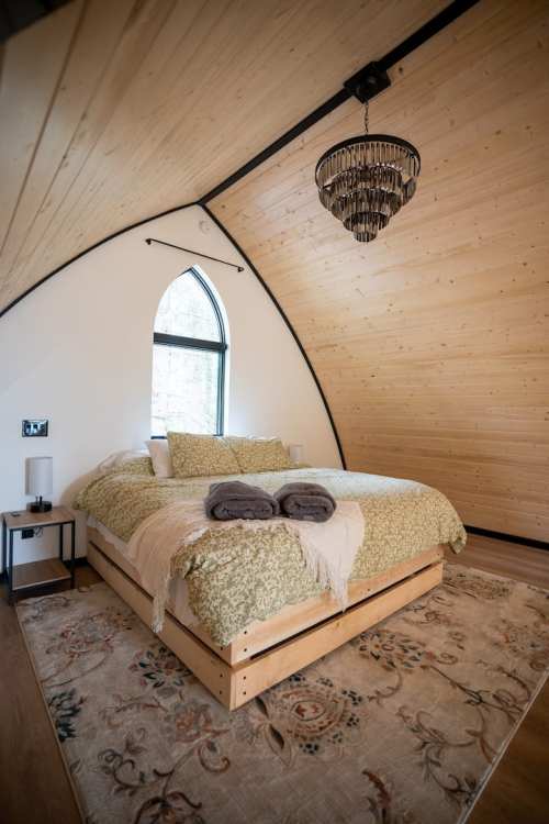 Cozy bedroom with a wooden ceiling, a large bed, decorative rug, and a stylish chandelier.