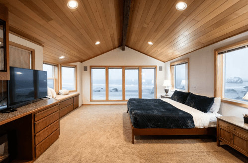 Cozy bedroom with a large window view of the ocean, featuring a bed, TV, and warm wooden accents.