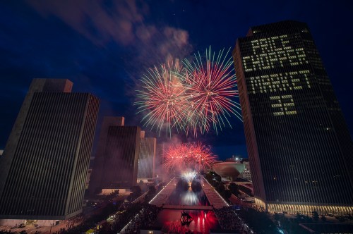 Colorful fireworks illuminate the night sky above tall buildings, celebrating a festive event in an urban setting.