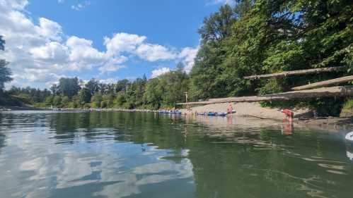 A serene river scene with people relaxing on the shore, surrounded by lush greenery and a partly cloudy sky.