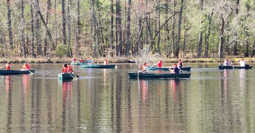 A group of people in canoes paddling on a calm lake surrounded by trees.