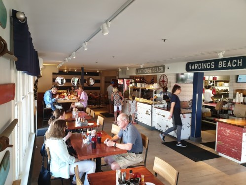 A busy restaurant interior with diners at tables, a counter area, and nautical-themed decor.