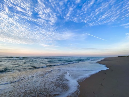 A serene beach scene at sunset, with gentle waves lapping at the shore under a sky filled with wispy clouds.