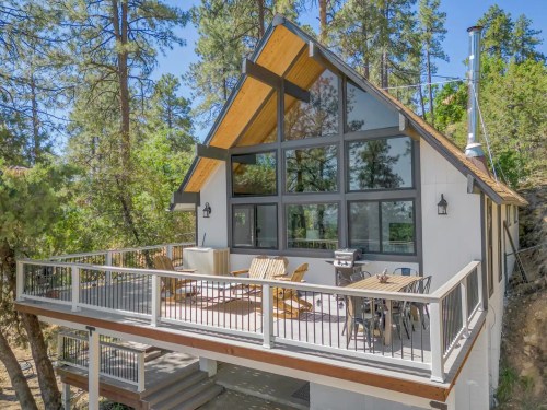 A modern cabin with large windows, a deck, and surrounded by trees, offering a serene outdoor space.
