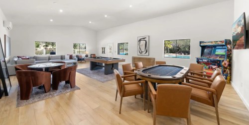Spacious game room with poker and pool tables, arcade machine, and comfortable seating. Bright, modern decor.