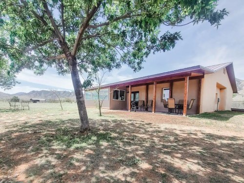 A cozy house with a porch, surrounded by trees and open land, under a clear sky.