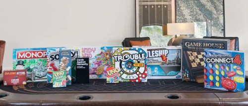 A collection of board games and card games displayed on a table, including Monopoly, Uno, and Connect 4.