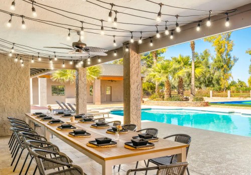 Outdoor dining area with a long table, string lights, and a pool surrounded by palm trees. Bright and inviting atmosphere.