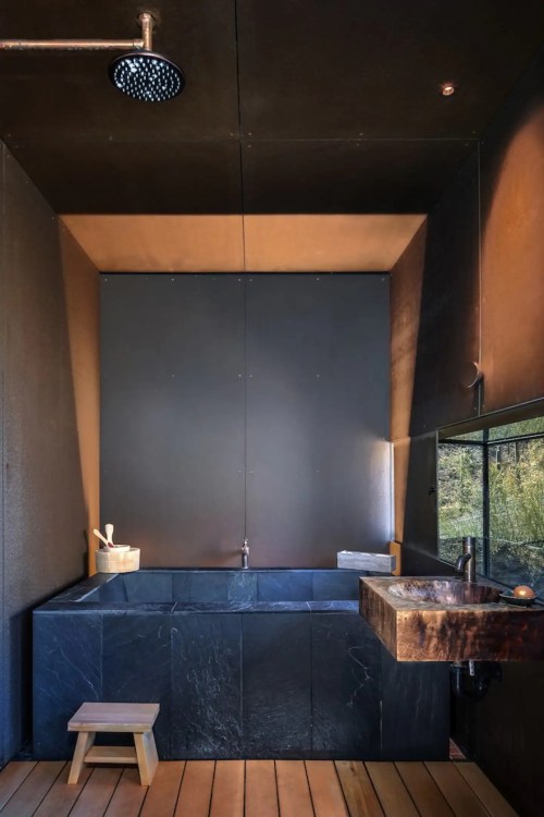 Modern bathroom featuring a sleek black tub, wooden accents, and a minimalist design with a rain shower.