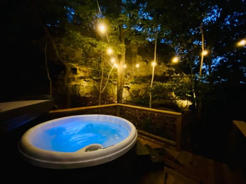 A serene hot tub surrounded by trees, illuminated by string lights at dusk.