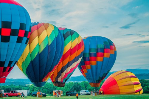 Colorful hot air balloons inflate on a grassy field under a blue sky, with people and vehicles nearby.