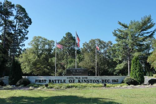 Sign marking the First Battle of Kinston, a Civil War site, with flags and trees in the background.