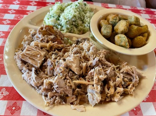 A plate of shredded meat, green rice, and fried okra on a checkered tablecloth.