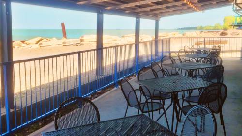 Outdoor seating area with black tables overlooking a lake and rocky shoreline under a covered patio.
