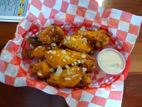 A basket of buffalo chicken wings drizzled with sauce and topped with cheese, served with a side of ranch dressing.