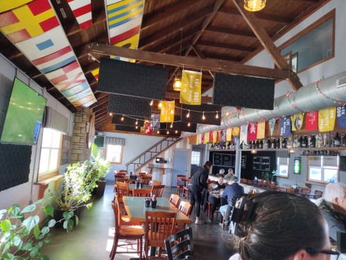 Interior of a restaurant with wooden beams, flags hanging from the ceiling, and patrons seated at tables.