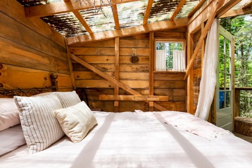 Cozy wooden interior of a treehouse bedroom with a bed, natural light, and rustic decor.