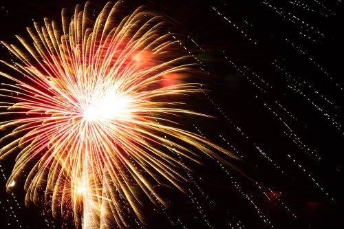 Colorful fireworks burst in the night sky, creating a vibrant display of red, gold, and white against a dark background.