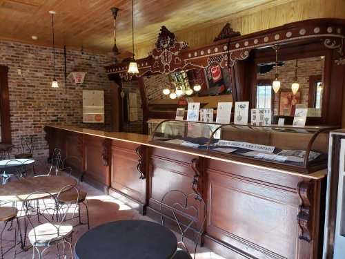A vintage-style café interior with a wooden counter, brick walls, and decorative lighting, featuring small tables and chairs.