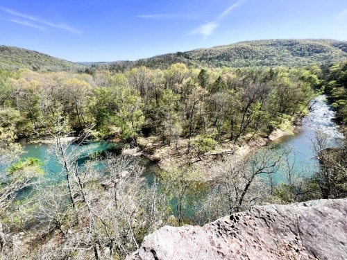 A scenic view of a winding river surrounded by lush green trees and rolling hills under a clear blue sky.