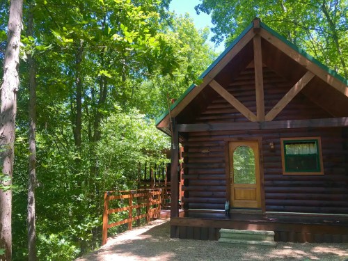 A cozy log cabin surrounded by lush green trees and a wooden walkway.