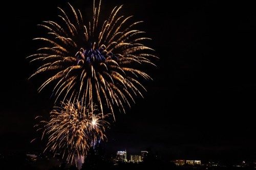 Colorful fireworks burst in the night sky over a city skyline, illuminating the dark backdrop.