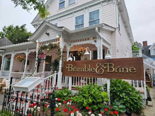 A charming pink Victorian house with a sign reading "Bramble & Brine" and colorful flowers in the foreground.