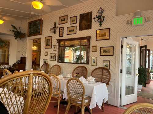 Cozy restaurant interior with white tablecloths, wicker chairs, and vintage framed art on the walls.